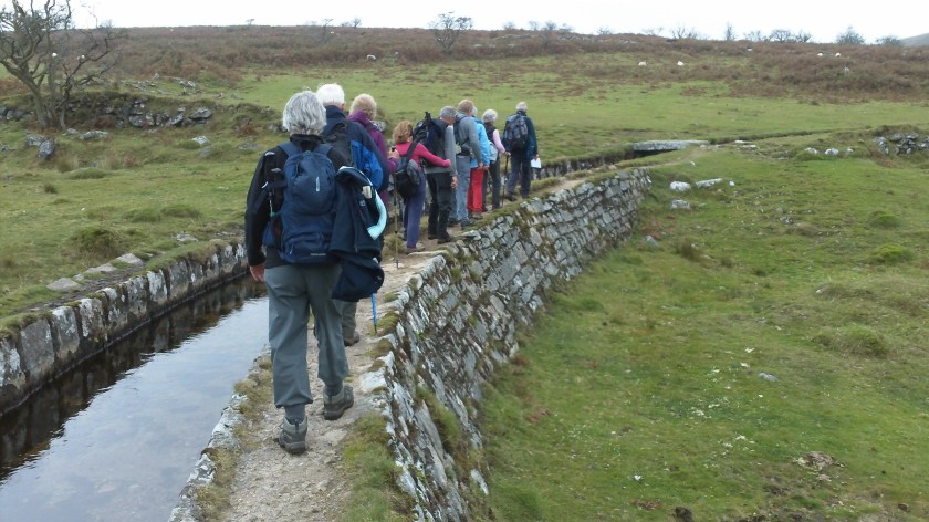 Group walking carefully alongside an ancient Leat on top of its supporting wall.